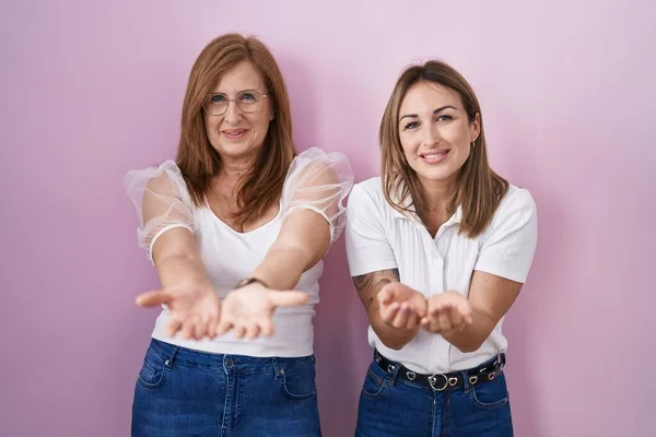 西班牙裔母亲和女儿穿着宽松的白色T恤 背景粉红 双手托着手 微笑着接受或给予的手势 持有和保护 — 图库照片