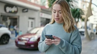 Sokakta akıllı telefon kullanan, kendine güvenen genç sarışın kadın.