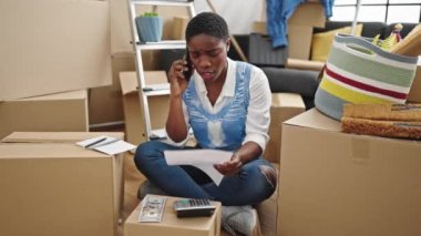 Afro-Amerikalı bir kadın yeni evinde akıllı telefon okuyarak konuşuyor.