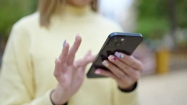 Young blonde woman using smartphone at park