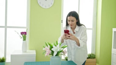 Genç, güzel, İspanyol bir kadın yemek odasında akıllı telefon kullanıyor.