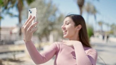Genç ve güzel İspanyol kadın gülümsüyor. Kendine güveni tam. Sokakta akıllı telefonun yanında selfie çekiyor.