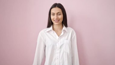 Genç ve güzel İspanyol kadın gülümsüyor. Kendine güveni tam. Başparmağıyla pembe arka plan üzerinde işaret veriyor.