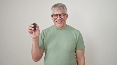 Orta yaşlı, gri saçlı, gülümseyen, kendine güveni tam, izole beyaz arka planda, yeni arabanın anahtarını işaret eden adam.