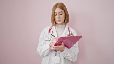 Genç sarışın kadın doktor not defterine yazıyor. Tecrit edilmiş pembe arka planda konuşuyor.