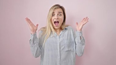 Young blonde woman standing with surprise expression over isolated pink background