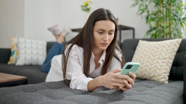年轻美丽的惊慌失措的女人用智能手机躺在家里的沙发上 — 图库视频影像