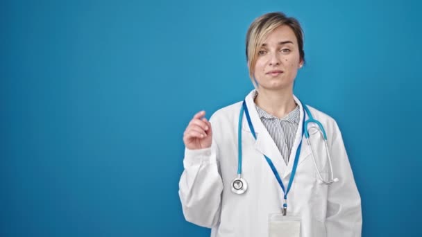 Joven Rubia Doctora Sonriendo Señalando Lado Sobre Fondo Azul Aislado — Vídeo de stock