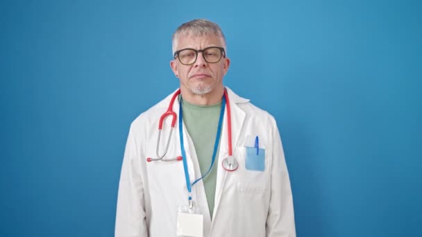 中年白发苍苍的男医生 手托着胸膛在孤零零的蓝色背景下宣誓 — 图库视频影像
