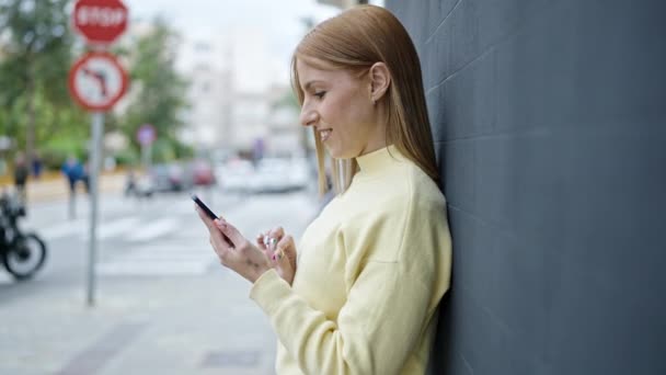 年轻的金发女人在街上用智能手机充满自信地微笑 — 图库视频影像