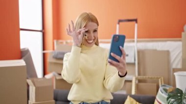 Young blonde woman having video call holding keys at new home