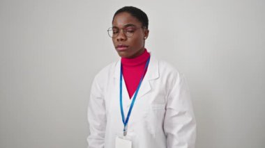 Afrika kökenli Amerikalı kadın doktor ciddi bir ifadeyle dikiliyor ve izole beyaz arka plan üzerinde steteskop takıyor.