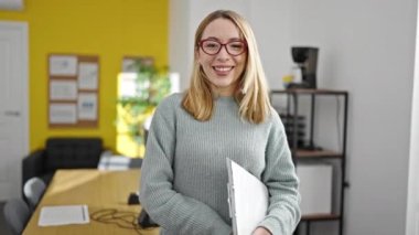 Young blonde woman business worker smiling confident holding clipboard at office