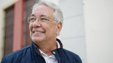 Orta yaşlı, gri saçlı, kendine güvenen bir adam caddeye bakıyor.