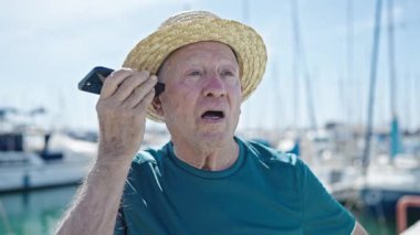 Yaşlı, kır saçlı, yaz şapkalı turist limandaki akıllı telefondan sesli mesaj dinliyor.