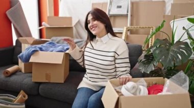 Genç, güzel İspanyol bir kadın, kendine güvenen bir şekilde koltukta oturuyor ve yeni evinde kollarını kavuşturup el kol hareketi yapıyor.