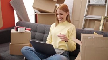 Young blonde woman having video call holding keys at new home