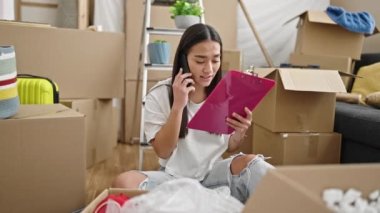 Genç, güzel İspanyol bir kadın yeni evdeki akıllı telefon okuma dokümanlarını tartışarak karton kutuları açıyor.