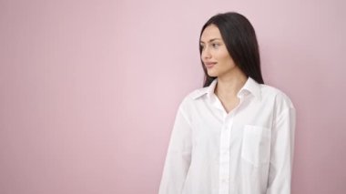 Genç, güzel, İspanyol bir kadın gülümsüyor. Kendine güveni tam, pembe arka planda parmaklarıyla işaret ediyor.