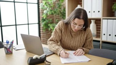Genç, güzel İspanyol iş kadını. Ofisteki evraklarda dizüstü bilgisayar kullanıyor.