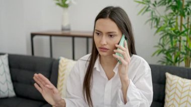 Genç, güzel, İspanyol bir kadın evde ciddi bir ifadeyle akıllı telefondan konuşuyor.