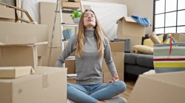 Genç beyaz kadın yoga egzersizi yapıyor. Yeni evinde yerde oturuyor.