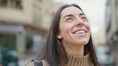 Young beautiful hispanic woman smiling confident looking to the sky at street