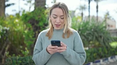 Parkta akıllı telefon kullanan, kendine güvenen genç sarışın kadın.