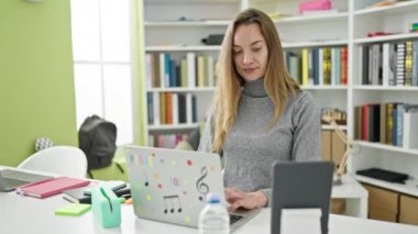 Kütüphane üniversitesinde okuyan genç, beyaz bir kız öğrenci dizüstü bilgisayar ve dokunmatik ped kullanıyor.