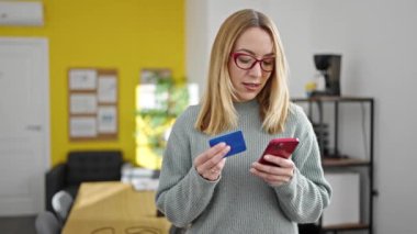 Genç sarışın iş kadını akıllı telefon ve kredi kartıyla alışveriş yapıyor.