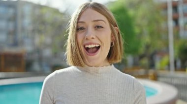 Young blonde woman standing with surprise expression at park