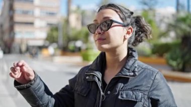 Parkta güneş gözlüğü takan, ciddi bir ifadeyle duran genç, güzel İspanyol bir kadın.