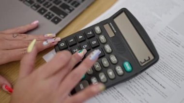 Ofiste dizüstü bilgisayar ve hesap makinesi kullanan bir kadın