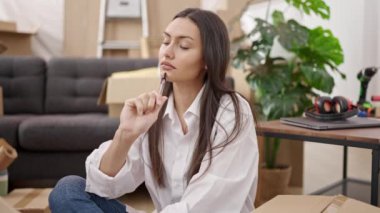 Genç, güzel, İspanyol bir kadın yeni evinde şüpheli bir ifadeyle yerde oturuyor.