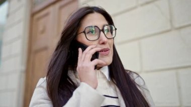 Genç, güzel, İspanyol bir kadın gülümsüyor ve caddede akıllı telefondan konuşuyor.