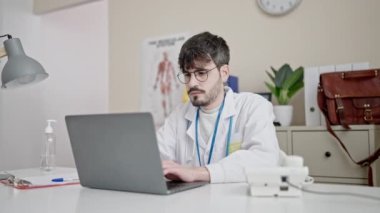 Young hispanic man doctor using laptop working at clinic