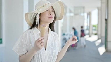 Genç Çinli kadın turist gülerek sokakta dondurma yiyor.