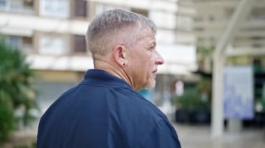 Middle age grey-haired man standing with serious expression at street