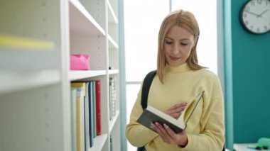 Young blonde woman student smiling confident reading book at university classroom