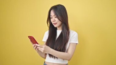 Akıllı telefon kullanan genç Çinli kadın izole edilmiş sarı arka planda gülümsüyor.