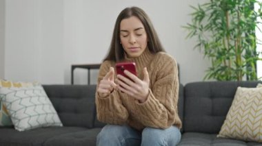 Genç ve güzel İspanyol kadın evde stresli bir ifadeyle akıllı telefon kullanıyor.