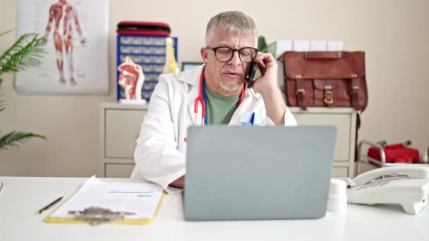Médico Cabelos Grisalhos Meia Idade Usando Laptop Falando Smartphone Clínica — Vídeo de Stock