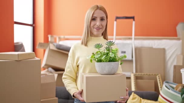 Young Blonde Woman Smiling Confident Holding Package Plant New Home — Video
