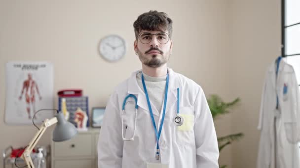 年轻的惊慌失措的医生微笑着在诊所用手做心脏手势 — 图库视频影像
