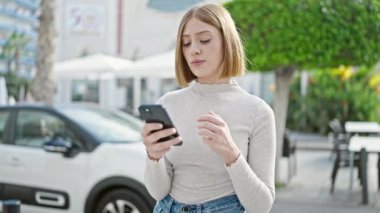 Kahve dükkanının terasında akıllı telefon kullanan genç sarışın kadın.