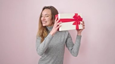 Kafkasyalı genç bir kadın pembe arka planda kendine güvenen bir doğum günü hediyesi sesi duyuyor.