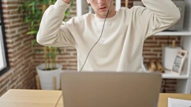 Genç beyaz adam yemek odasında dizüstü bilgisayar ve kulaklık kullanıyor.