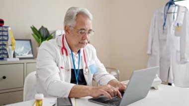 Klinikte laptopunu kullanan gri saçlı orta yaşlı bir adam.