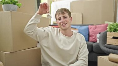 Elinde yeni evin anahtarları olan beyaz bir adam yeni evinde konuşuyor.