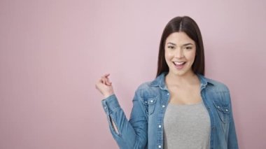 Young beautiful hispanic woman smiling confident pointing with finger to the side over isolated pink background